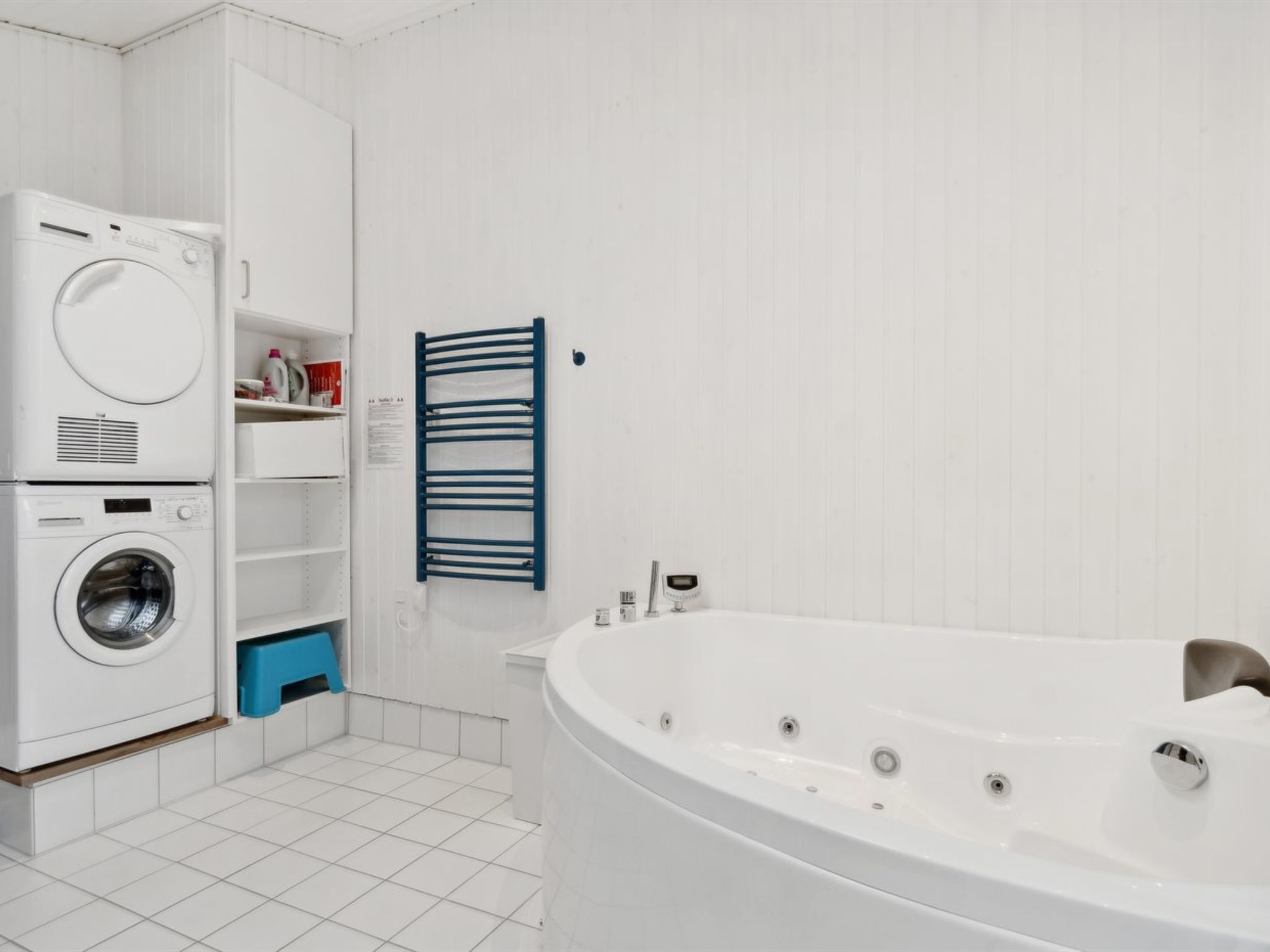 Un baño con una bañera blanca, lavadora y secadora apiladas, y un perchero azul.