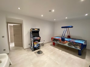 A room with a pool table, a gaming machine, and a door leading to another room. - ✨ Maison Calypso – Luxury Lakefront Villa with Hot Tub & Sauna (GERARDMER)