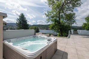 A hot tub on a patio with a view of a tree and distant hills.