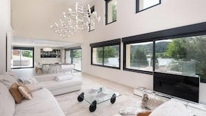 A spacious living room with a large flat-screen TV, a glass coffee table, and a modern chandelier. - ✨ Maison Calypso – Luxury Lakefront Villa with Hot Tub & Sauna (GERARDMER)