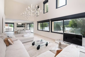 A spacious living room with a large flat-screen TV, a glass coffee table, and a modern chandelier. - ✨ Maison Calypso – Luxury Lakefront Villa with Hot Tub & Sauna (GERARDMER)