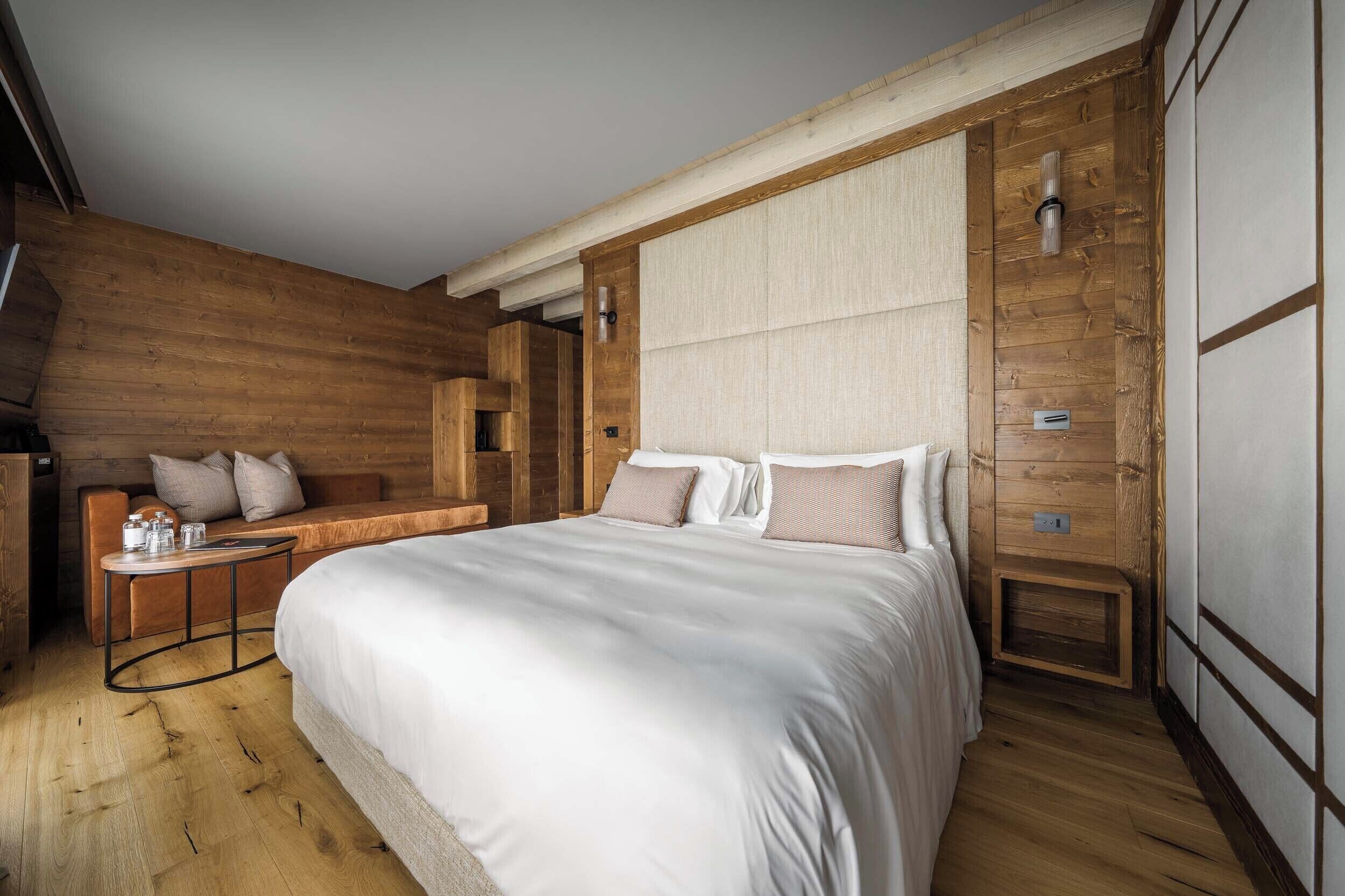 A bedroom with a large bed, wooden walls, a small table with a lamp, and a bench with cushions.