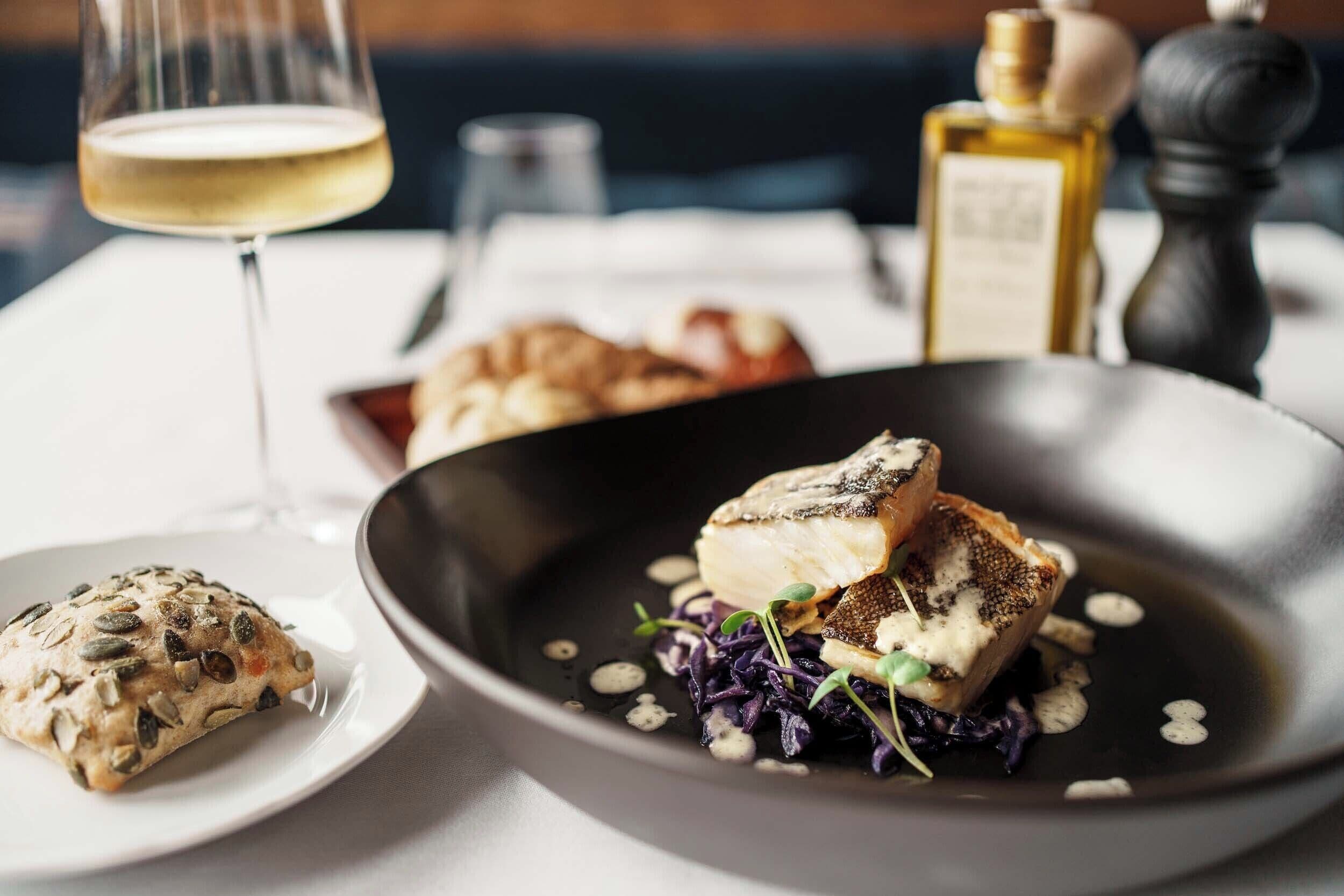 Un tavolo imbandito con un piatto di cibo, un bicchiere di vino bianco e una bottiglia d'olio d'oliva.