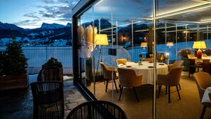 An outdoor dining area with a glass wall overlooking a snowy mountain range. - Casa Guargne' (Cortina d'Ampezzo)