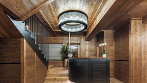 A wooden interior with a staircase, a black reception desk, and a chandelier. - Casa Guargne' (Cortina d'Ampezzo)