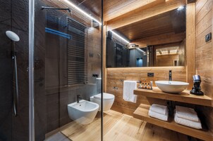 Un baño moderno con cabina de ducha de vidrio, un bidé, un inodoro y un mueble de tocador de madera con lavabo y toallero.
