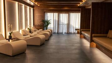 A spa room with reclining chairs, a massage table, and a large window with curtains.