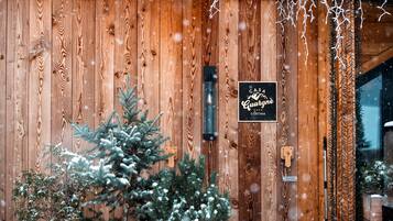 En entré till en stuga av trä, med ett snötäckt julgran och en skylt som lyder: ”Casa Quarengue Cortina”.