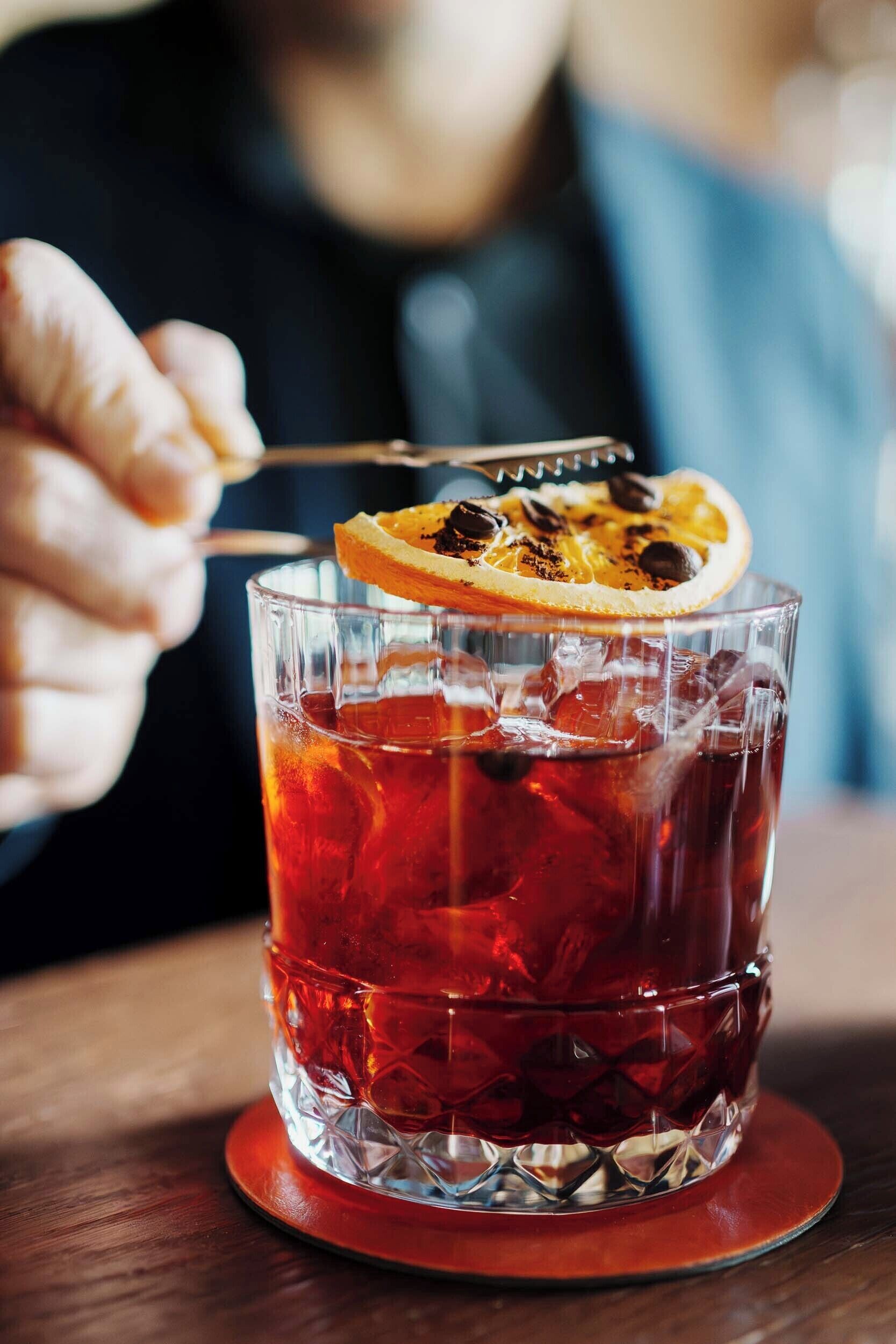 Ein Glas rotes Getränk mit Eiswürfeln und einem Orangenschnitzchen am Rand.