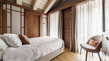 A bedroom with a bed, a chair, wooden beams, and curtains.