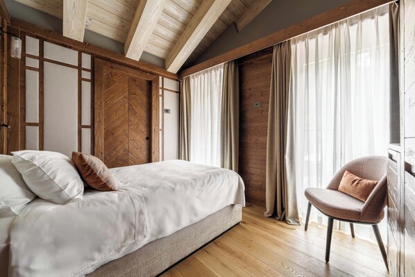 Un dormitorio con cama, una silla, vigas de madera y cortinas.