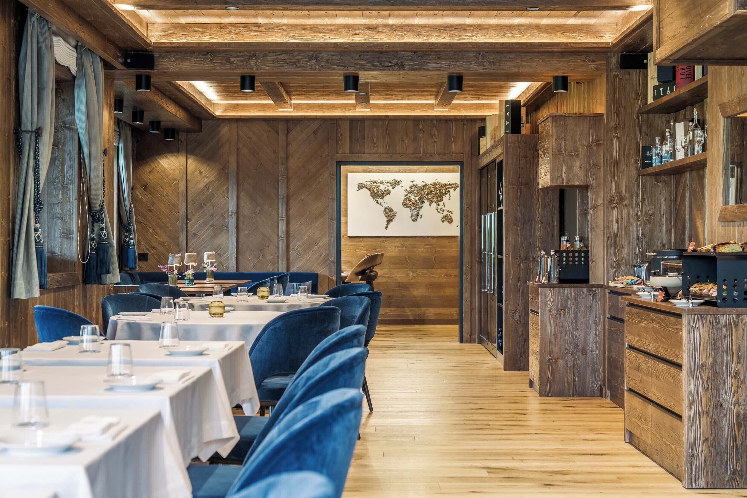 Ein Restaurant mit Holzwänden, einer Weltkarte als Wandmalerei und blau gepolsterten Stühlen.