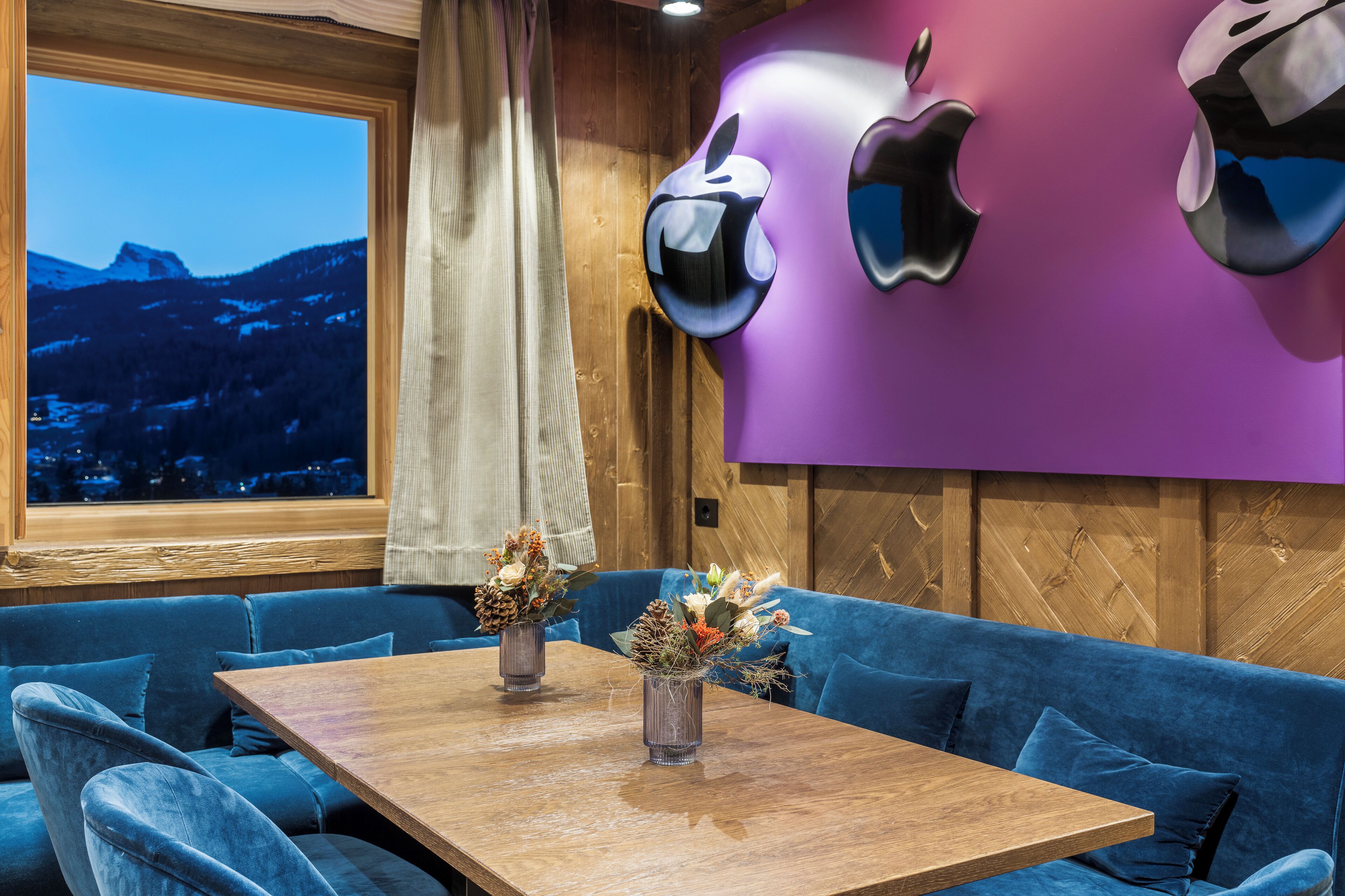 Um interior moderno com uma parede de madeira, o logotipo roxo da Apple, uma mesa de madeira e sofás azuis.