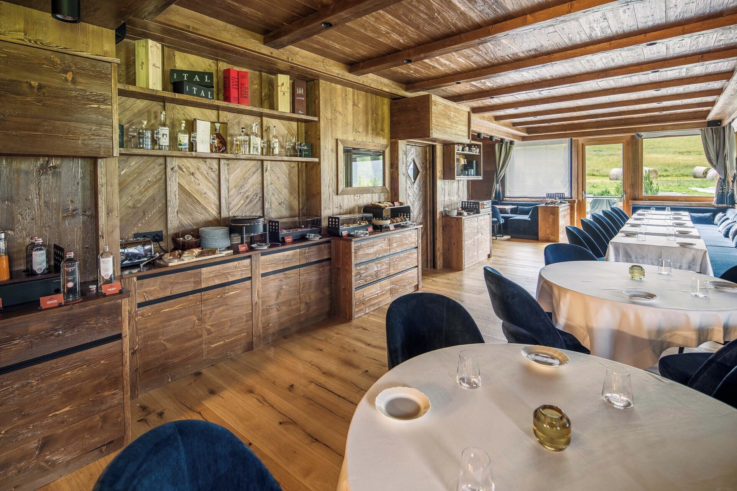 Un intérieur rustique en bois, avec un espace bar, des sièges pour prendre les repas et de grandes fenêtres offrant une vue sur l’extérieur.