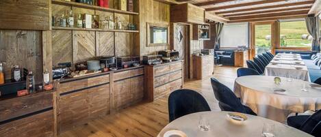 Un interior rústico de madera con barra, asientos para comer y grandes ventanales con vistas al exterior.