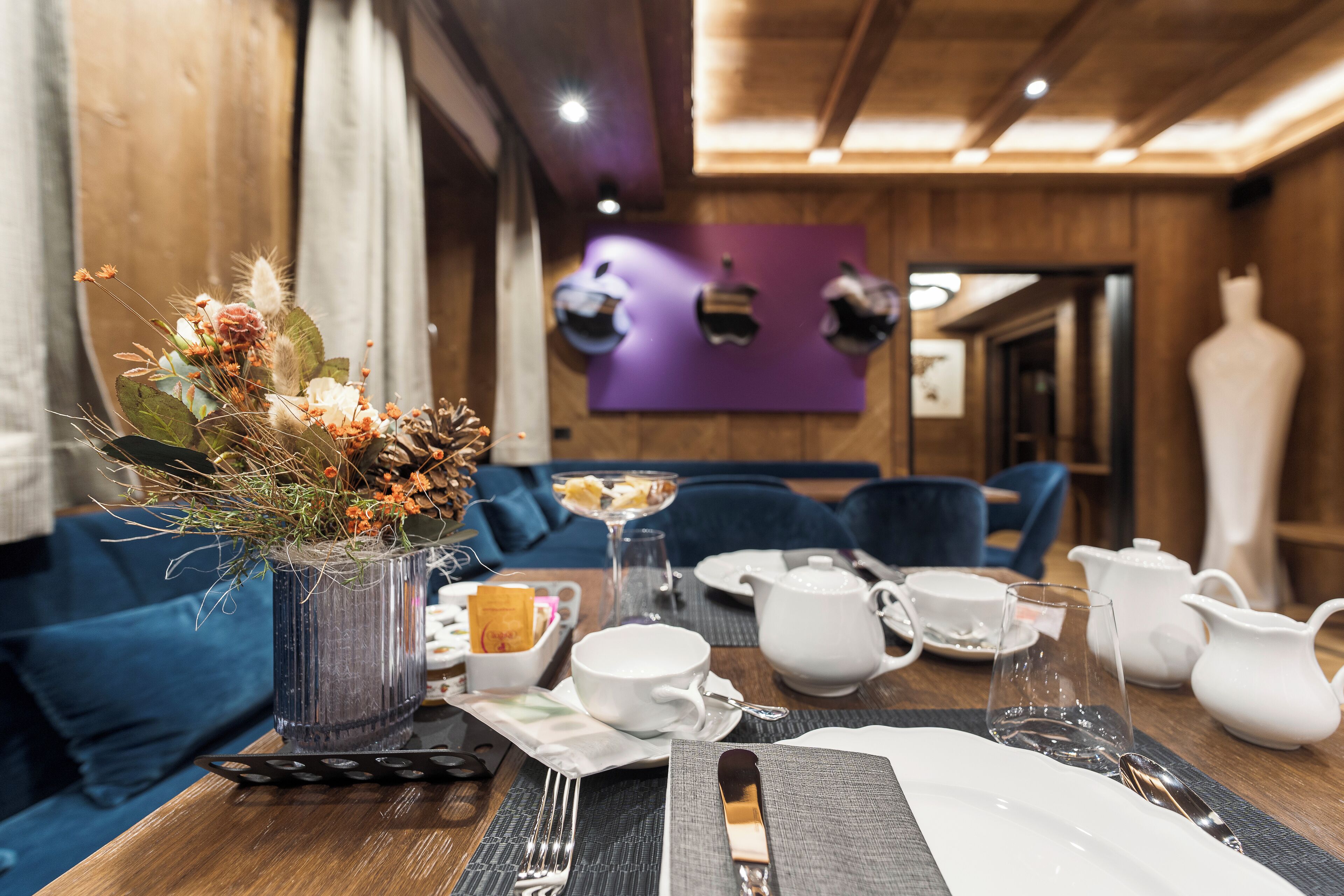Una mesa de comedor dispuesta con vajilla blanca, un florero con flores secas y un vaso de vidrio transparente.