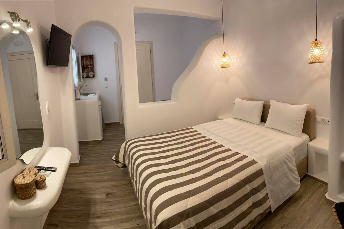 A bedroom with a bed, bedside tables, a TV, and a bathroom with a sink and mirror.