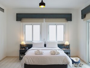 A hotel room with a large bed, two bedside tables with lamps, a window with blinds, a pet bed, and a small table with a bowl. - Tsanotel Hotel (Limassol)