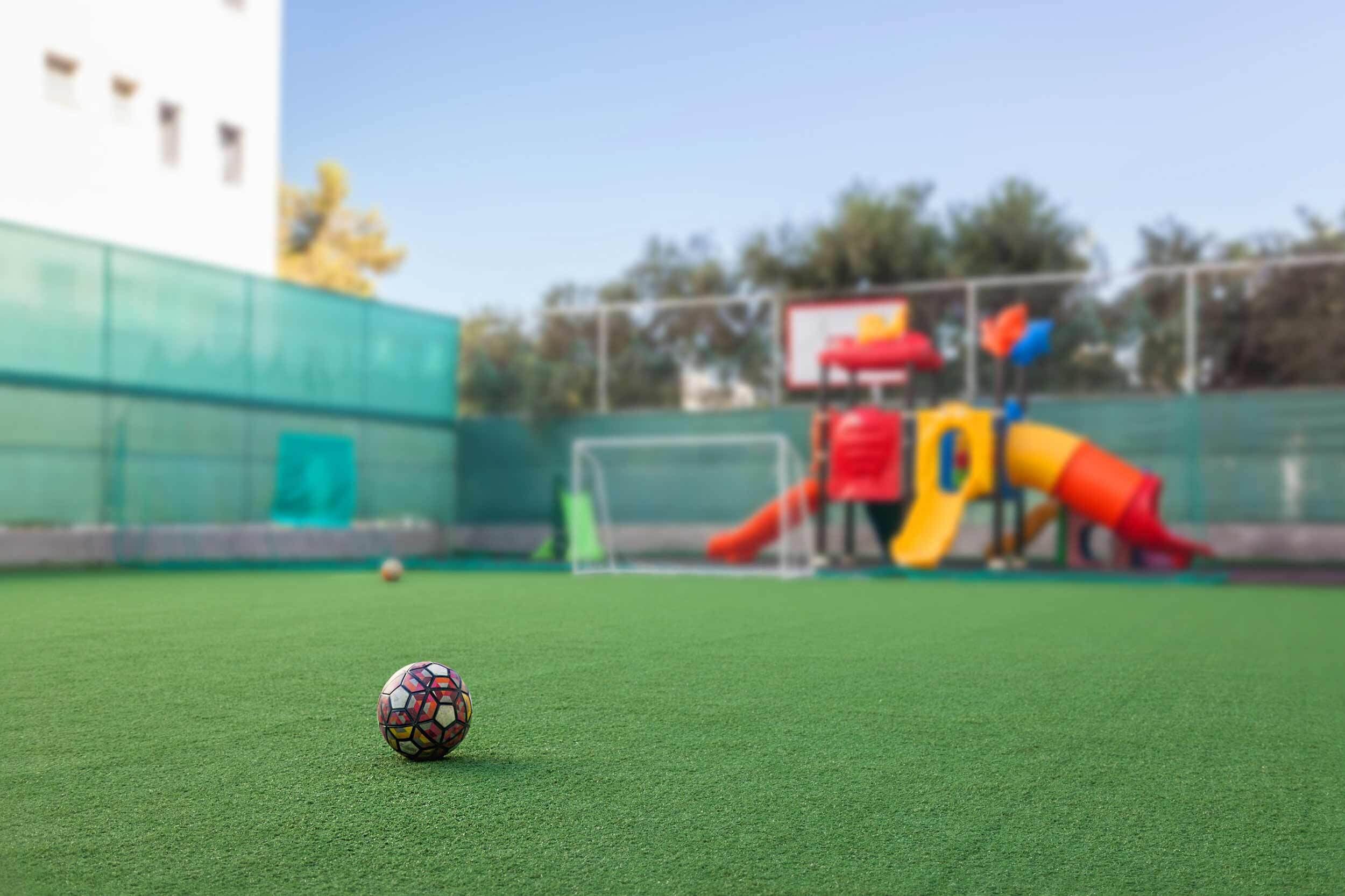 A soccer ball on artificial turf with a playground in the background.