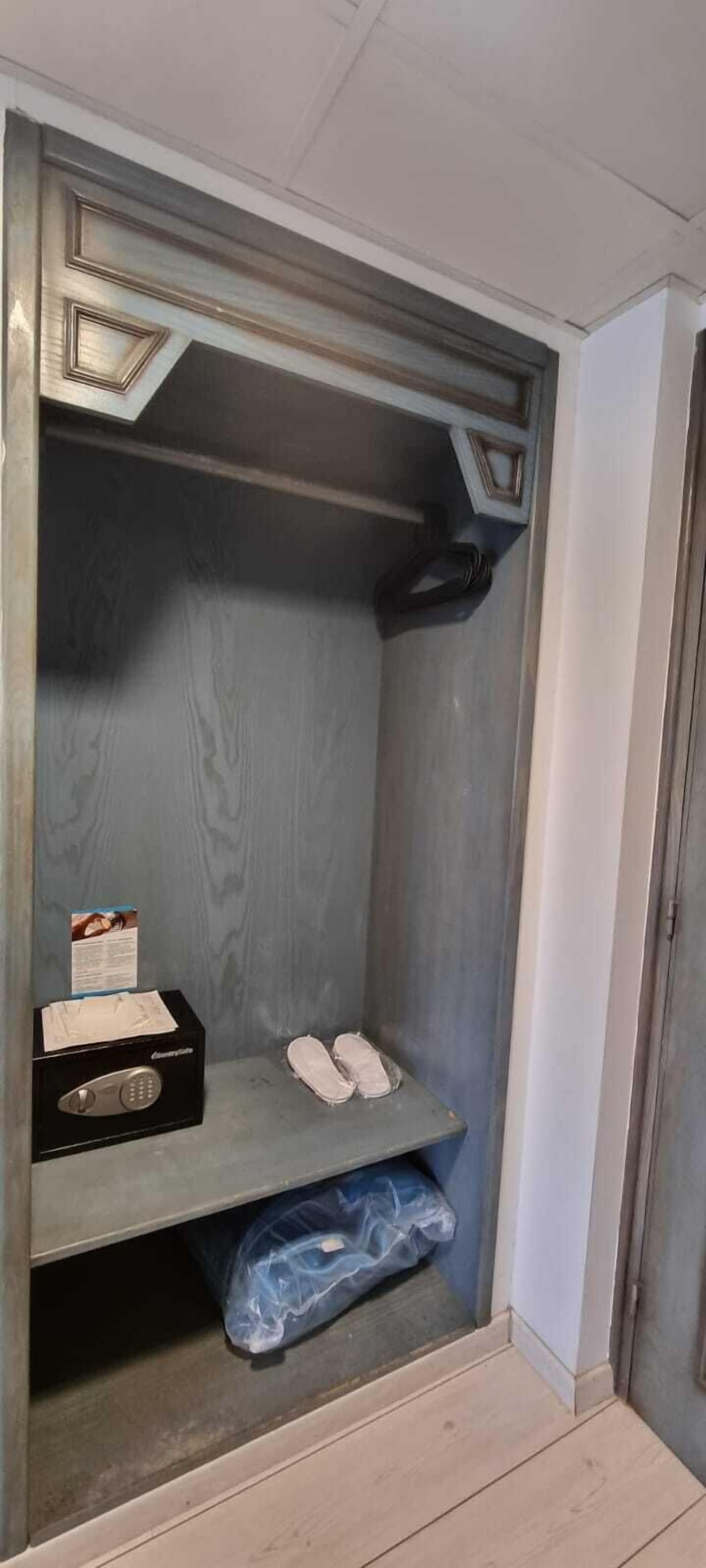 A small, enclosed storage space with a wooden door, a shelf with a box and a pair of shoes, and a blue plastic bag on the floor.
