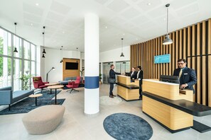 A modern hotel reception area with a wooden reception desk, a large pillar, and seating arrangements. - Holiday Inn Express & Suites Reims - Rives de Vesle (Reims)