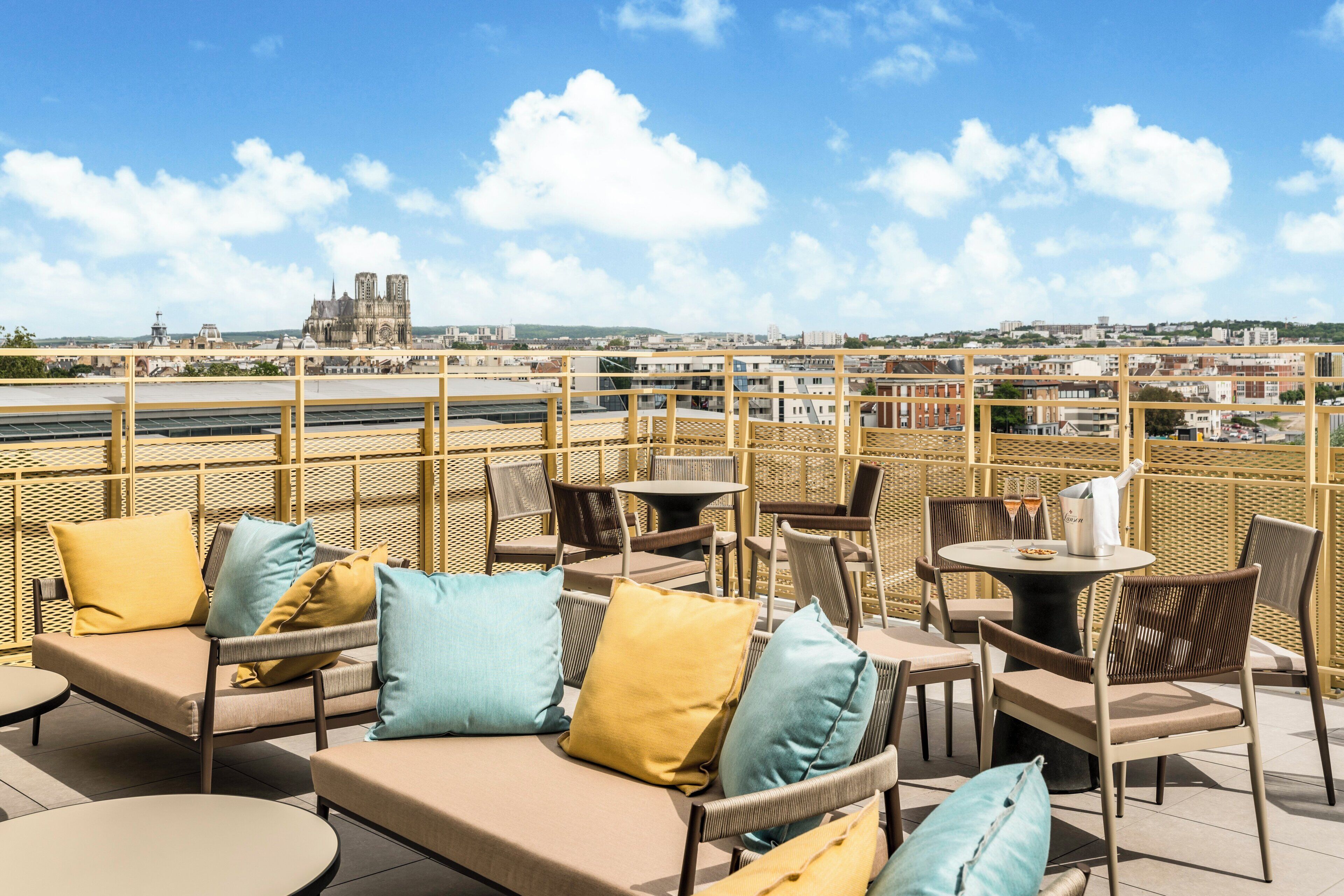 A rooftop terrace with outdoor seating, a view of a cathedral, and a cityscape in the background.