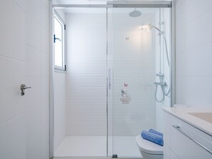 Une salle de bain moderne avec une douche à parois de verre, des toilettes et un lavabo surmonté d’une serviette bleue.