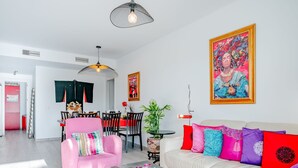 A modern living room with a pink armchair, a white sofa with colorful cushions, a coffee table with drinks, and a dining area in the background. - Marina Real I by Interhome (Dénia)
