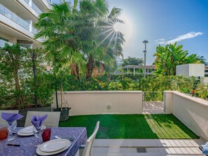 Une terrasse sur le toit aménagée avec un espace repas, des palmiers et une vue sur un bâtiment en arrière-plan.