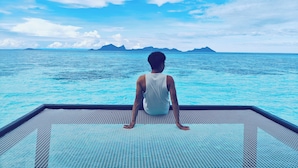 A person sitting on a poolside deck overlooking a clear blue sea with distant islands. - Bubblefish water villa (Semporna)