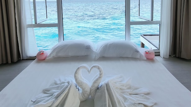A hotel room with a large bed, white linens, and a heart-shaped towel arrangement. - Bubblefish water villa (Semporna)