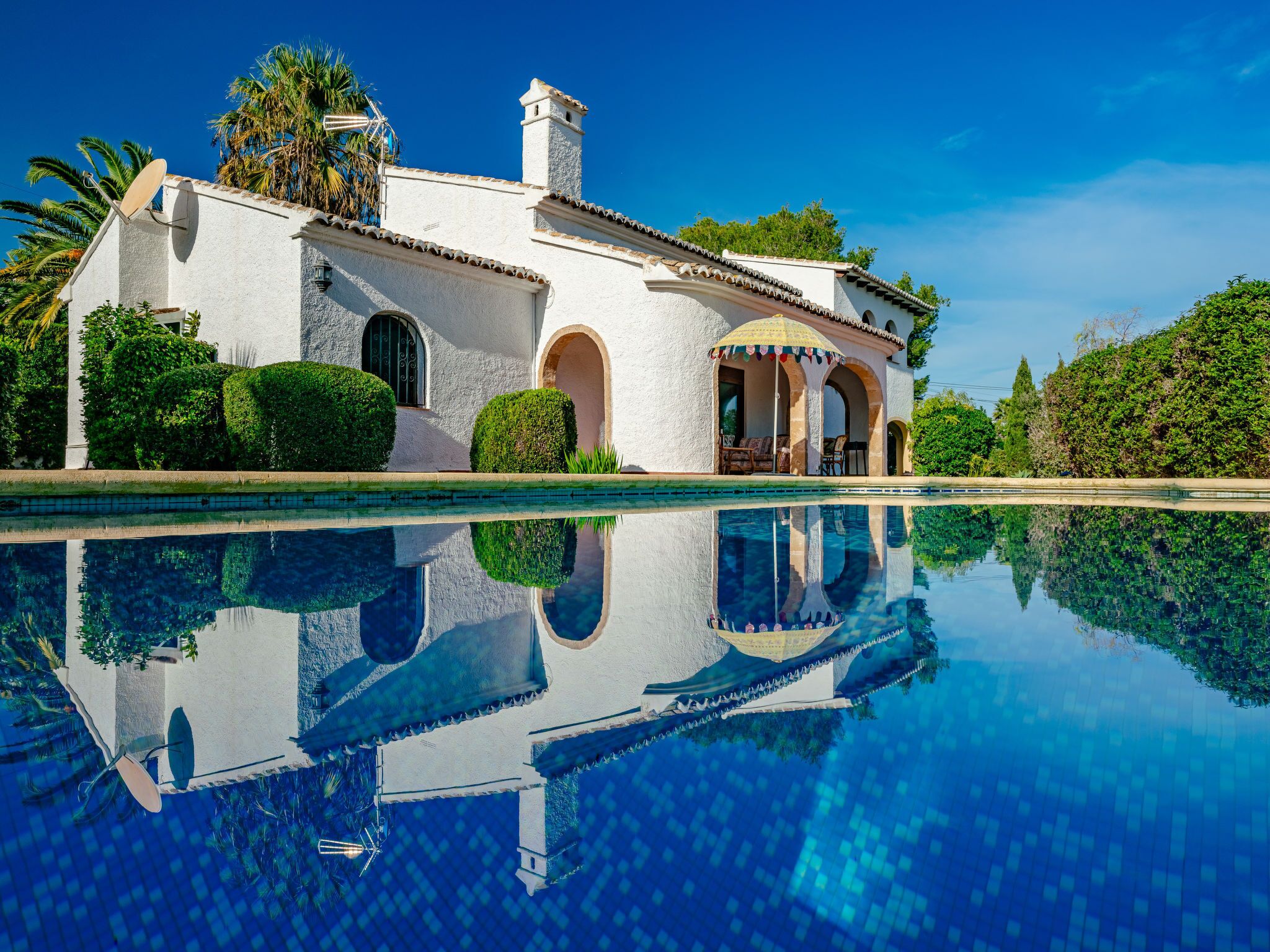 A white villa with a pool, arched windows, and a covered patio.