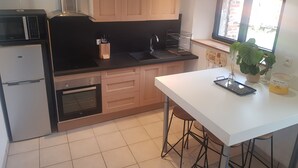 Een moderne keuken met een wit aanrecht, houten kastjes, een inbouwoven en een raam met uitzicht.