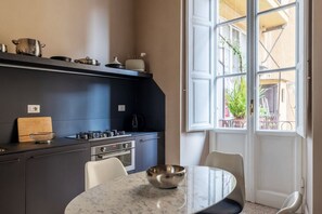 Eine moderne Küche mit Marmorarbeitsplatte, einem Esstisch mit Stühlen und einem großen Fenster mit Blick nach draußen.