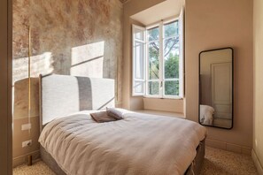 A bedroom with a large bed, a window with a view, and a mirror on the wall.