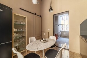 A compact kitchen with a dining area, a refrigerator, a glass cabinet with dishes, and a window with a view.