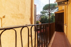 A narrow balcony with a metal railing, a tiled floor, and a view of a street with buildings and trees.