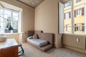A small, cozy room with a single bed, a desk, and a window with a view of buildings.