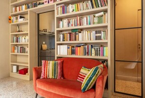 Ein rotes Sofa mit gestreiften Kissen vor einem Bücherregal voller Bücher.