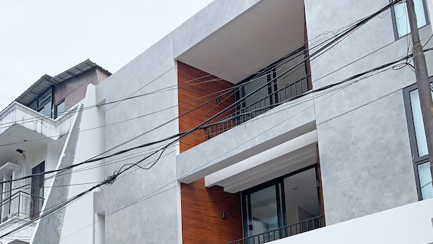 Un bâtiment moderne à deux étages, doté d’un grand portail de garage, d’un mur d’accent en bois et de plusieurs balcons.