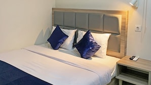Un lit bien fait, avec une tête de lit en bois, deux oreillers, une table de chevet sur laquelle se trouve une lampe et une télécommande.