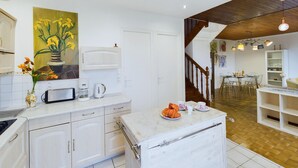 A modern kitchen with white cabinetry, a painting of flowers, and a dining area with a wooden staircase. - House for 5 to 50m from the seafront (Penmarch)