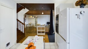 A compact kitchen with a white refrigerator, a dining area with a table and chairs, and a staircase leading to another level. - House for 5 to 50m from the seafront (Penmarch)