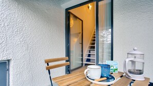 Un banco de madera con una taza blanca y una taza azul sobre una bandeja, un hervidor blanco y un libro titulado 'Verveine Menthe Bio' sobre una mesa.