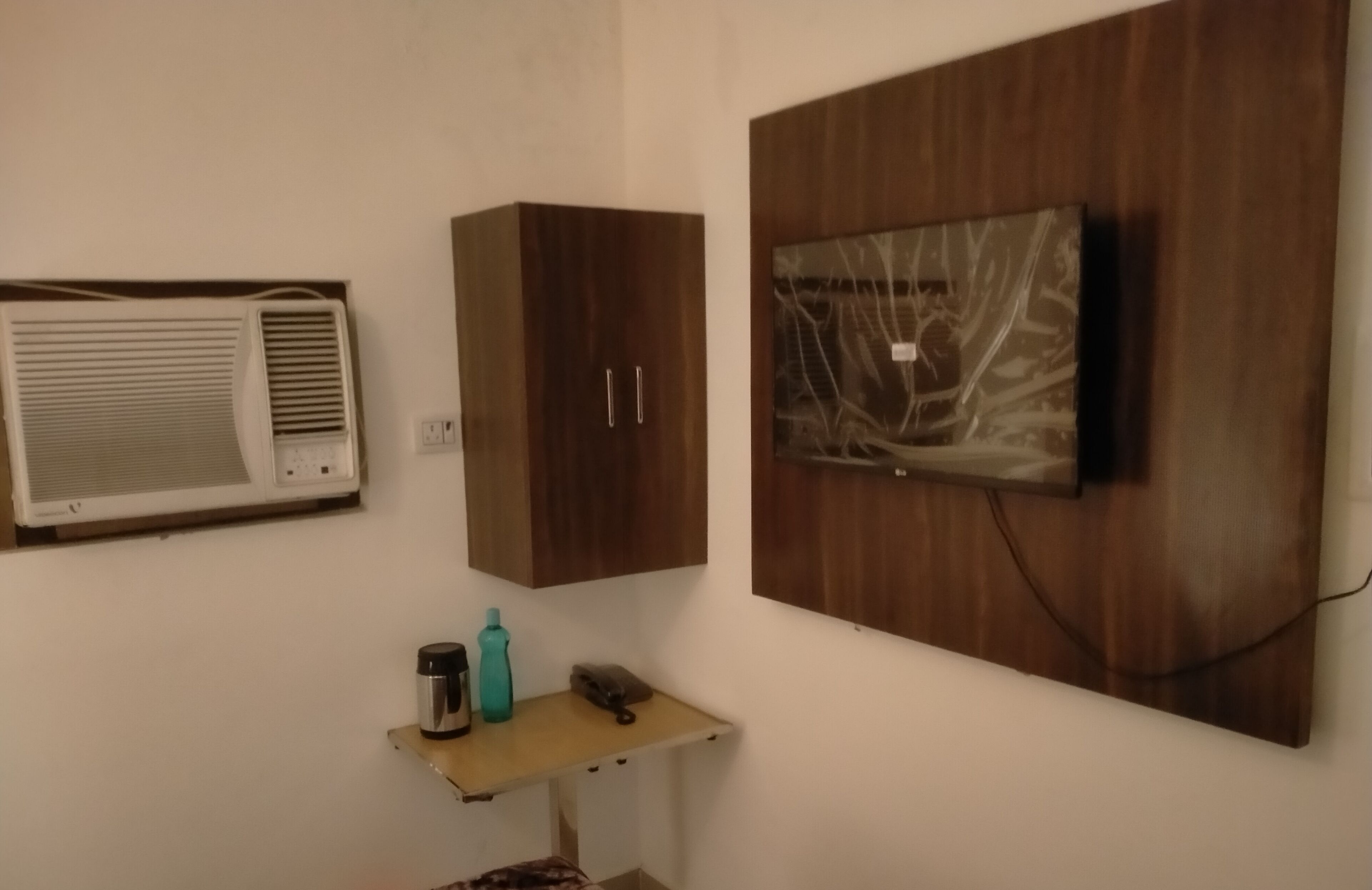 A room with a wall-mounted air conditioner, a wooden cabinet, and a TV on a wooden panel.