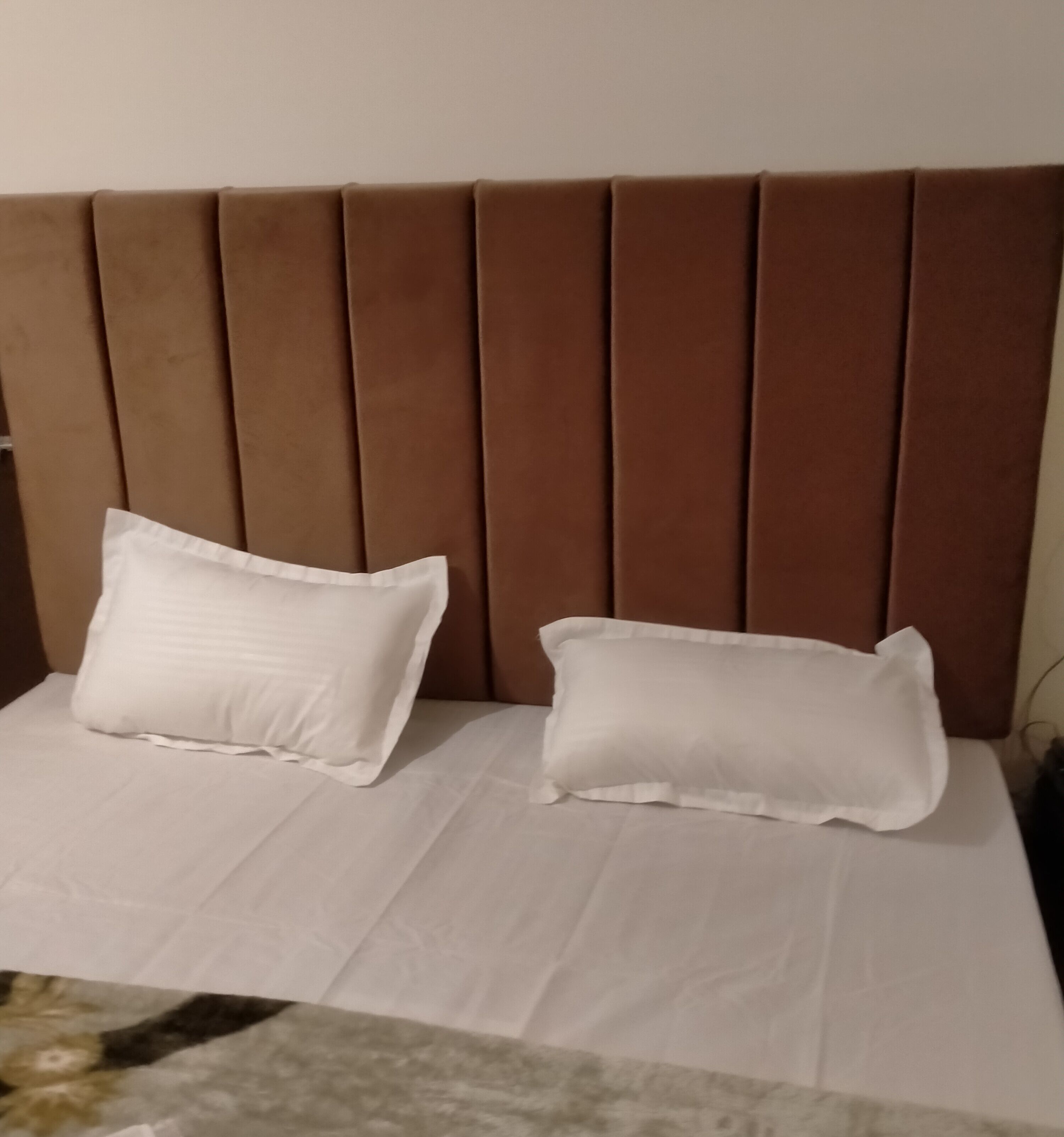 Uma cama com cabeceira marrom e duas almofadas brancas.