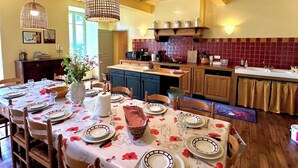 Een eetruimte met een tafel gedekt voor zes personen, een keuken op de achtergrond en een hanglamp.