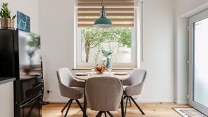 A dining area with a round table, two chairs, a hanging light fixture, and a window with blinds.
