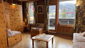 Ein gemütliches Zimmer mit Holzmöbeln, einer Couch, einem kleinen Tisch und einem Fenster mit Bergblick.