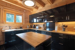 A modern kitchen with wooden cabinetry, a central island, and a window with a view of greenery. - Toison D'or - 8 pers. - Jacuzzi + sauna (Xonrupt-Longemer)